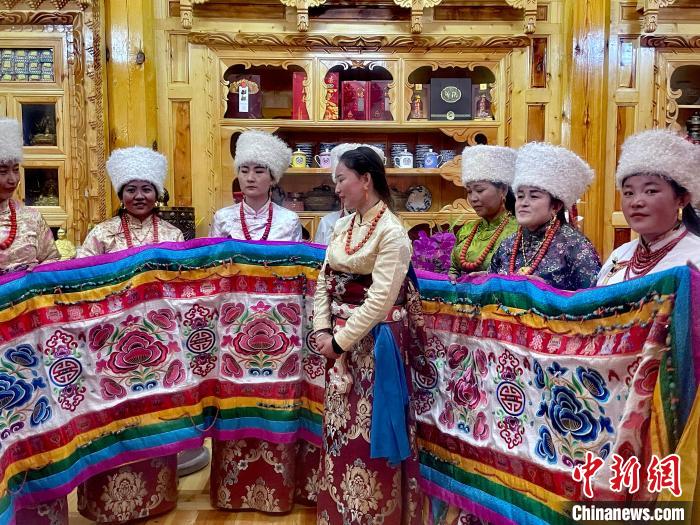 圖為女性展示村民自發(fā)繡制的“百米五彩哈達(dá)”。　李玉峰 攝